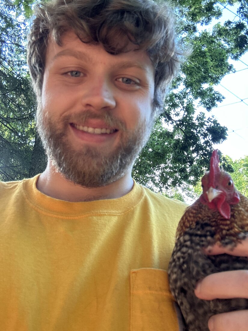 Nathan smiling with his bantam rooster under the trees