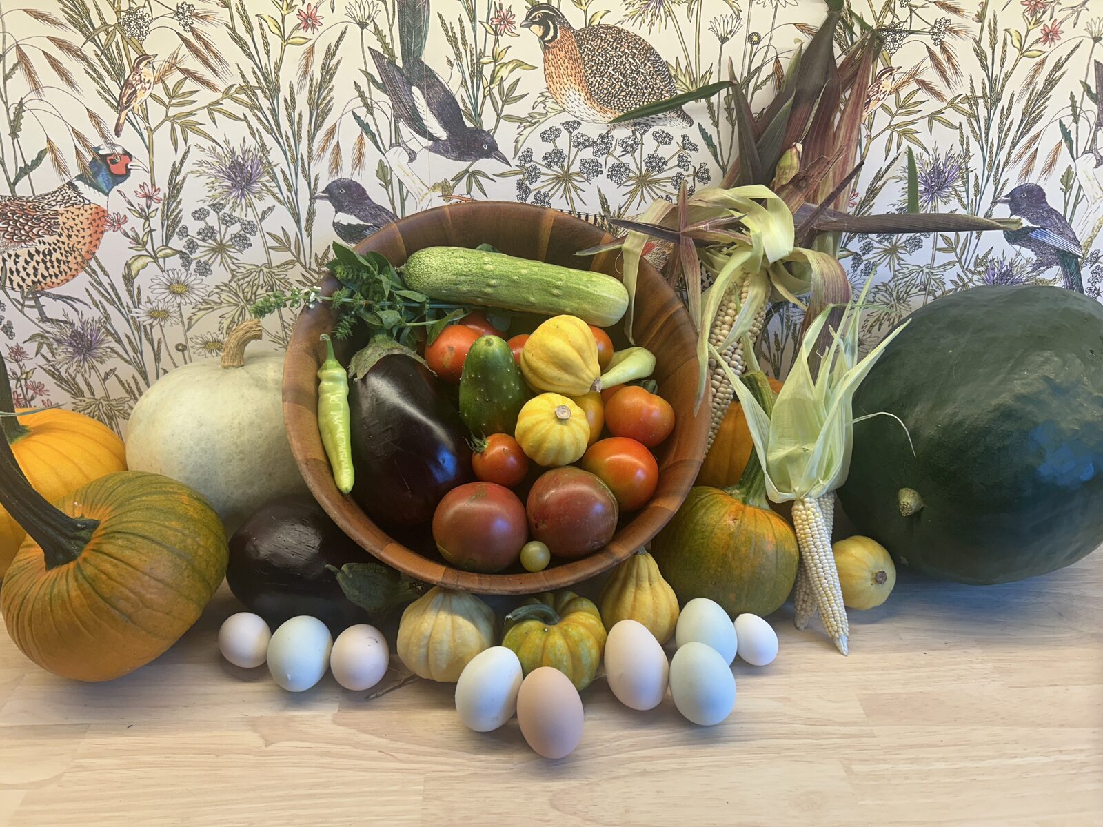 The week's squash harvest on the farm table beside fresh eggs